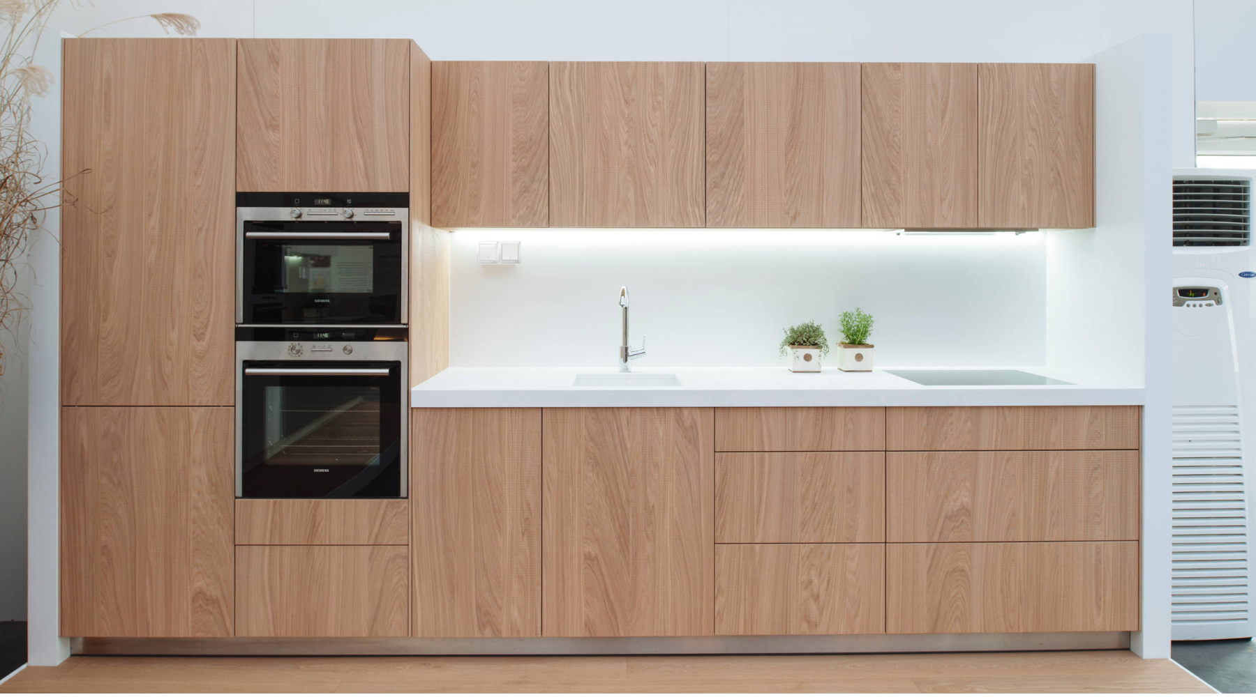 Modern minimalist wood grain kitchen in a Singapore BTO flat featuring a seamless white backsplash, under-cabinet LED task lighting, and sleek white designer light from Goldberg Home