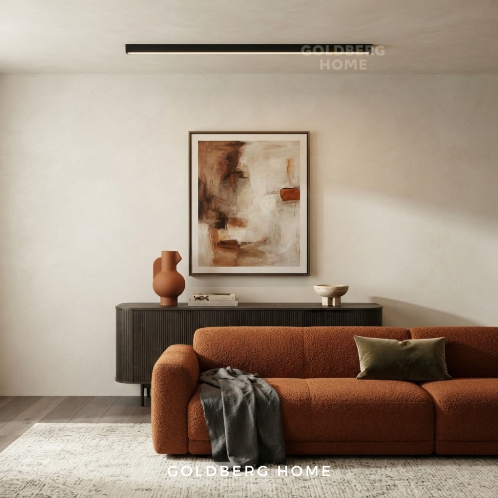 Goldberg Home Frankfurt black long rectangle LED ceiling light installed on ceiling above modern living room with rust orange sofa and framed wall art.